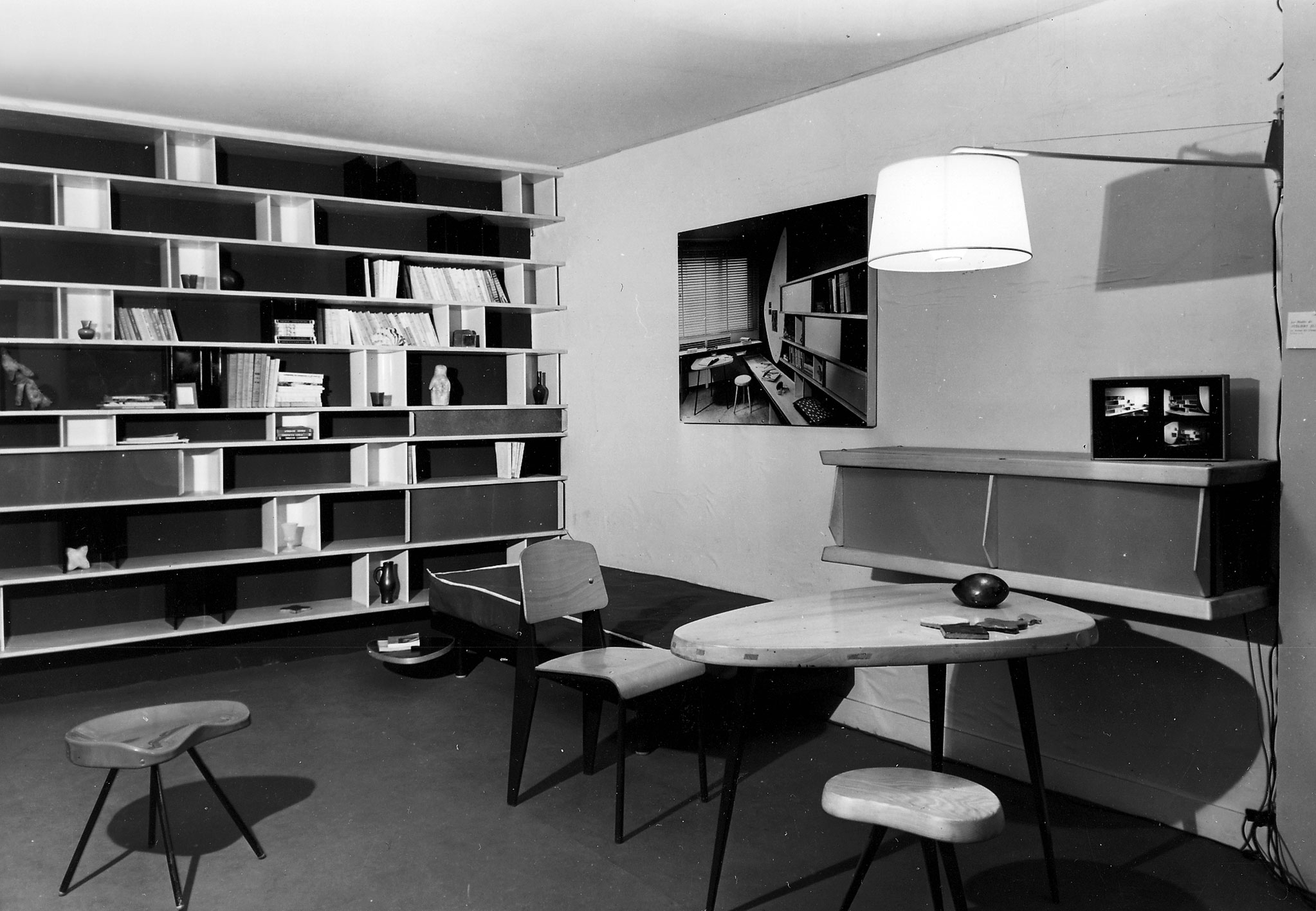Ateliers Jean Prouvé booth at the Salon des Arts Ménagers, 1953. Scenography by Charlotte Perriand. Furniture by Jean Prouvé: Métropole no. 305 chair, stool no. 307, swing-jib lamp, SCAL no. 450 bed (with a swiveling tablet by Charlotte Perriand). Furniture by Charlotte Perriand: large bookcase, free form table from the Maison du Mexique, free form stool, wall storage unit.